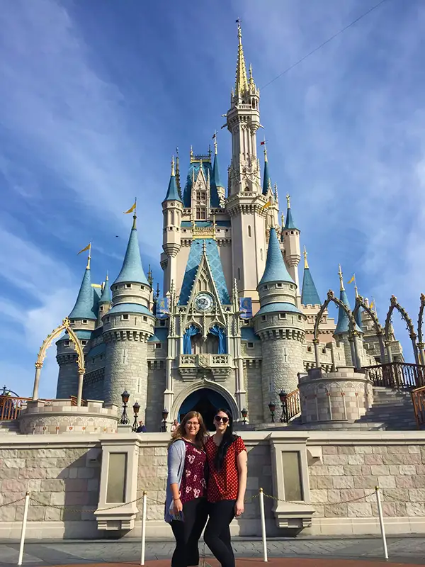 disney Two people stand happily in front of Cinderella Castle at Disney World, with a clear blue sky above.