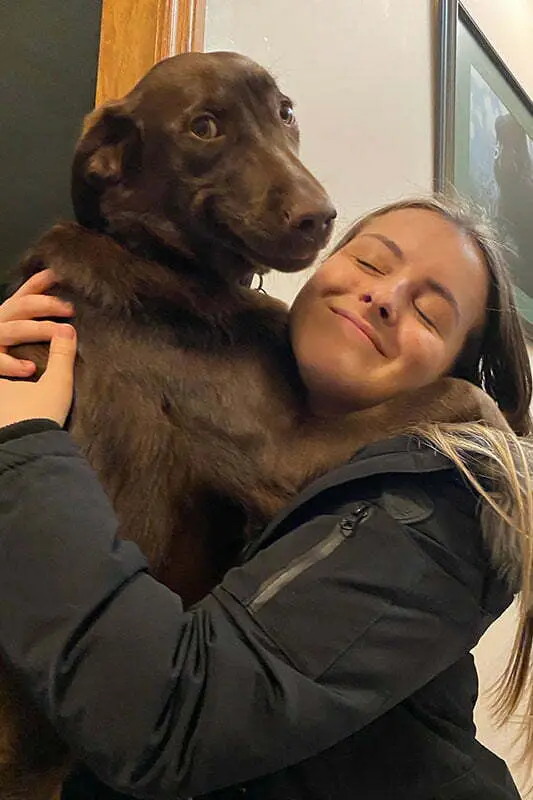 A person is joyfully hugging a large brown dog in a cozy indoor setting, conveying warmth and affection.