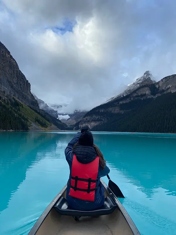 A person in a canoe paddles across Lake Louise, surrounded by stunning mountains under a dramatic cloudy sky.