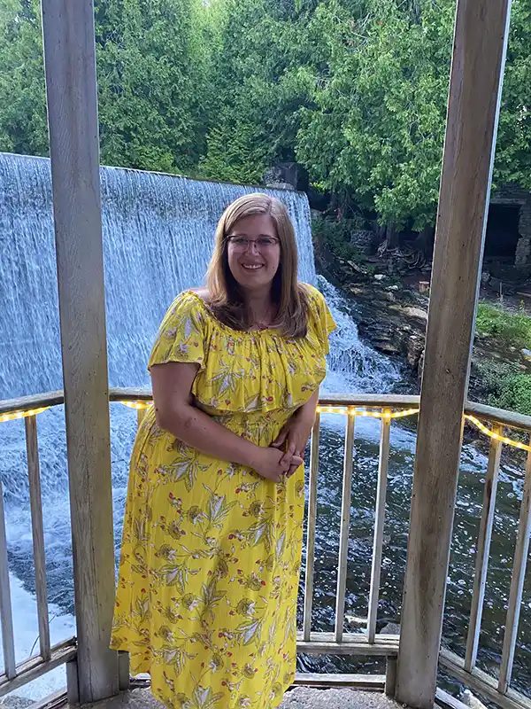 wedding-venue A person in a yellow dress stands on a gazebo overlooking a waterfall, surrounded by lush green trees and gentle flowing water.